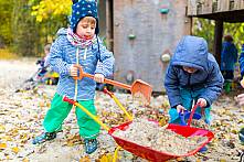 Zwei Jungen befüllen eine Schubkarre mit Sand